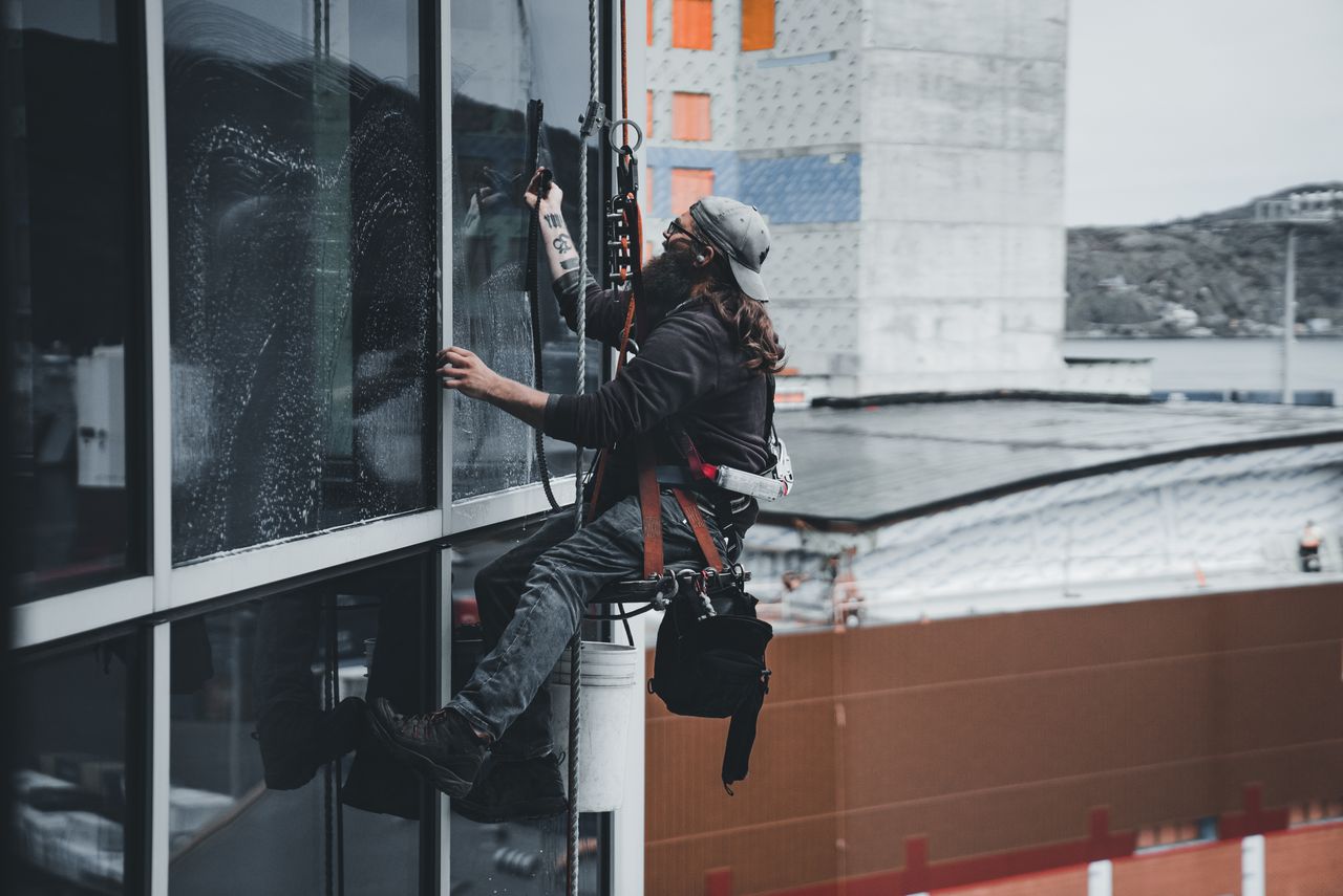 services-03 A man cleaning skyscraper windows with a harness, showcasing urban high-rise work.