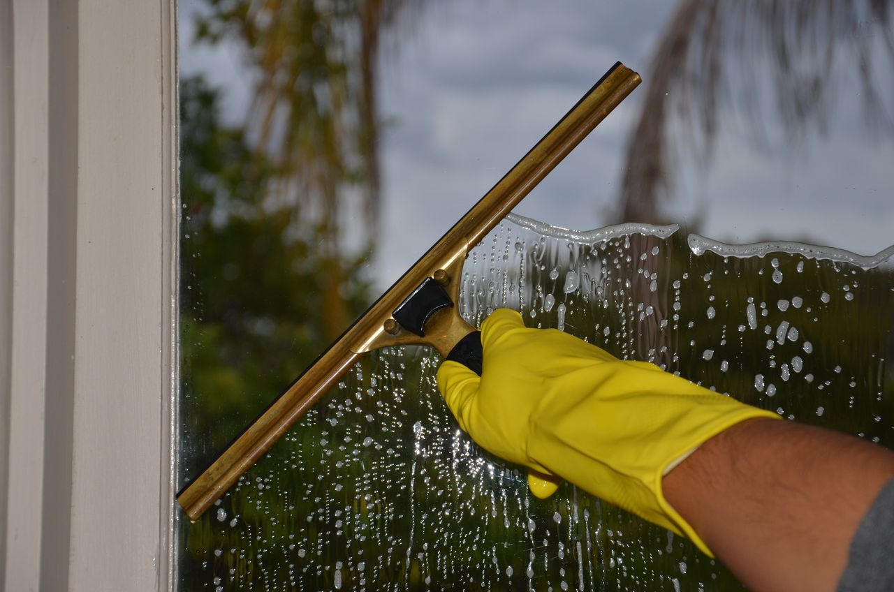about-img-01 Close-up of hand cleaning window with squeegee outdoors using yellow gloves.